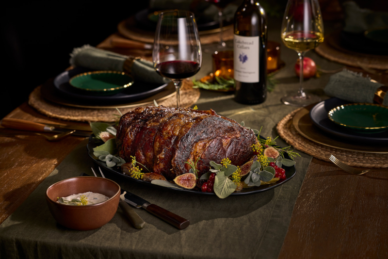 Rib roast on a festive plate on a wood table next to bowl of white cream sauce.