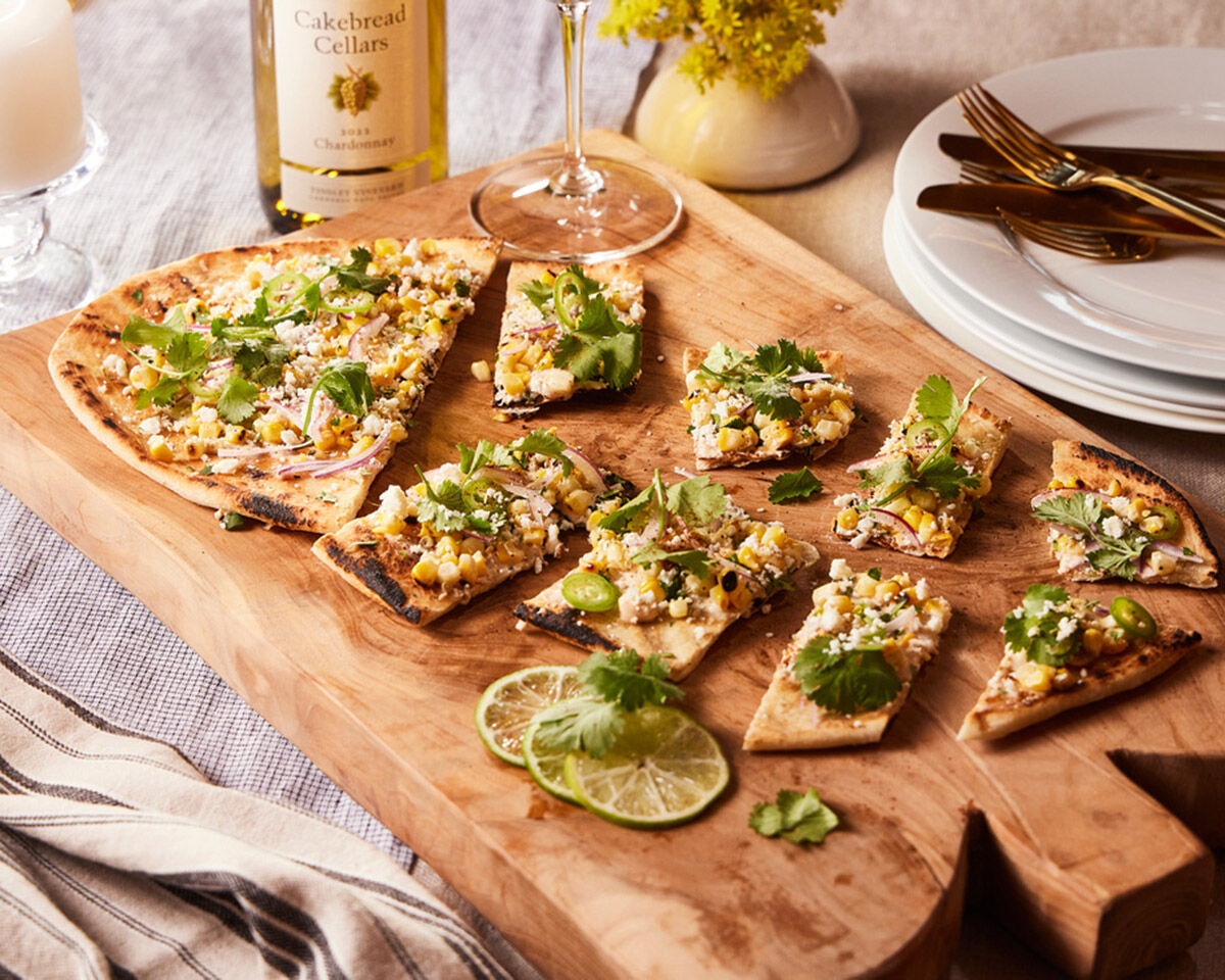 Delicious grilled Mexican street corn flatbread topped with cilantro and cheese on a wooden serving board. Perfect for flavor.