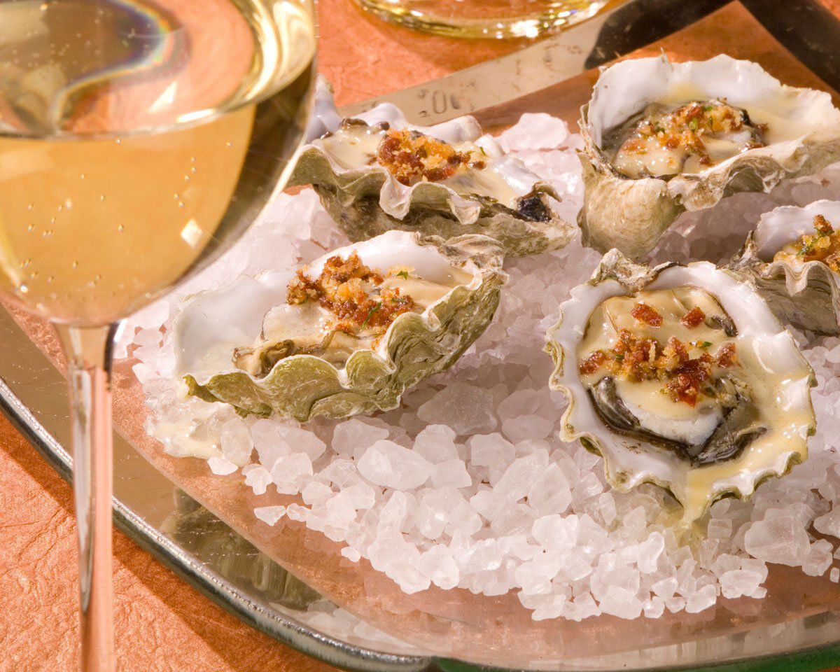 Fresh oysters on ice with a glass of white wine, served on a metal tray, highlighting a seafood dish paired with wine.