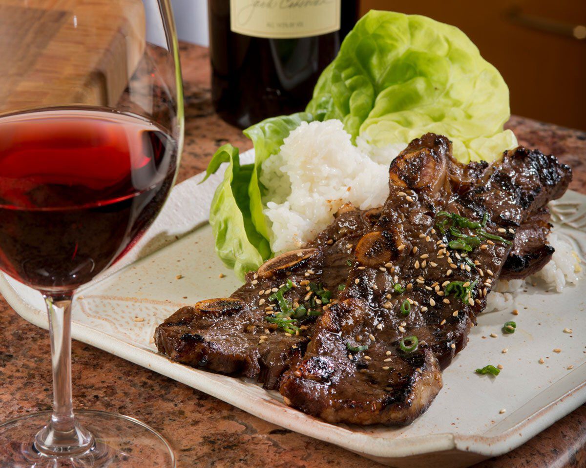 Korean-style barbecue beef with lettuce, rice, and a glass of red wine on a dinner plate.
