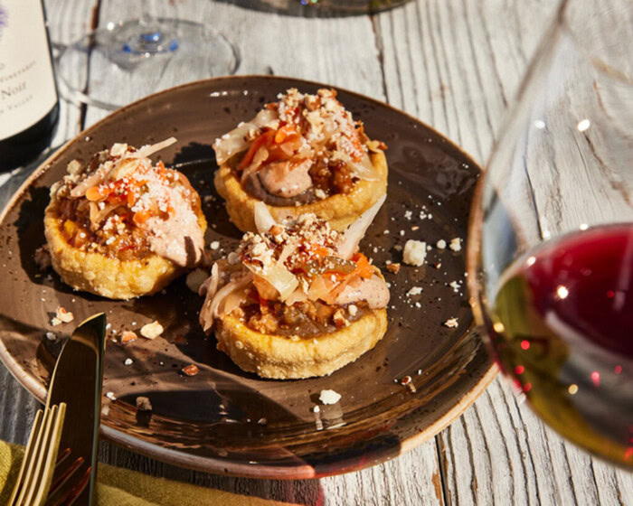 Mexican sopes topped with duck picadillo, pecan crema, and cheese on a dark plate, served with wine and rustic wooden table b.