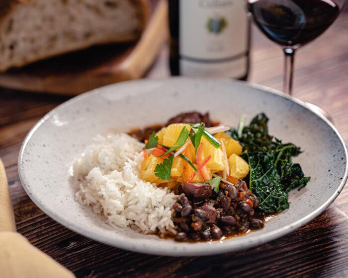 Scott's Brazilian Feijoada with black beans, smoked ham hocks, sausage, kale, and steamed rice on a rustic plate.
