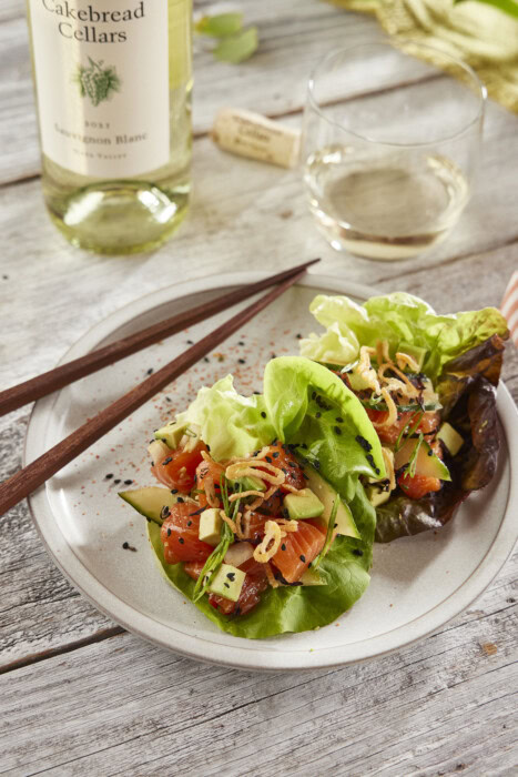 A detailed description of a spicy salmon poke served in lettuce cups, garnished with vegetables and herbs, on a rustic wooden.