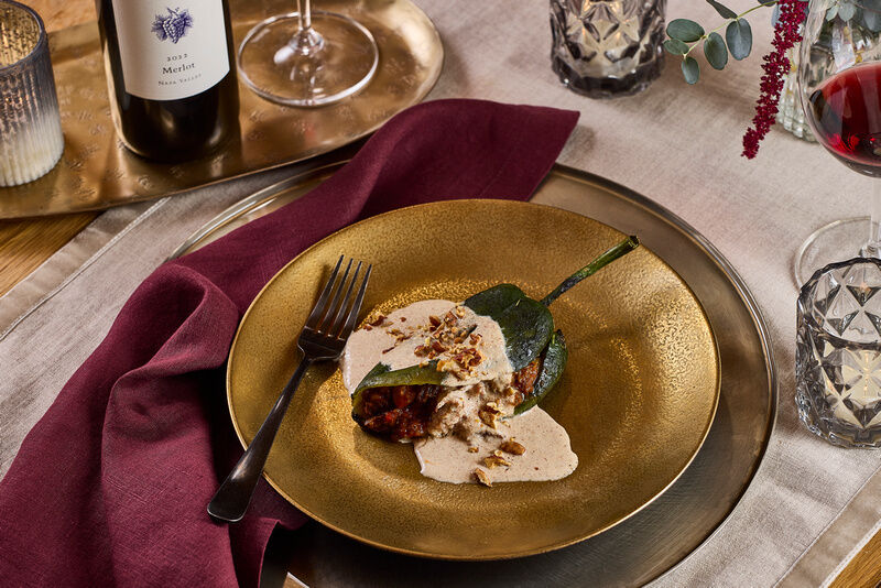 Roasted stuffed pepper with creamy sauce on a gold plate, wine glasses, and elegant table setting.