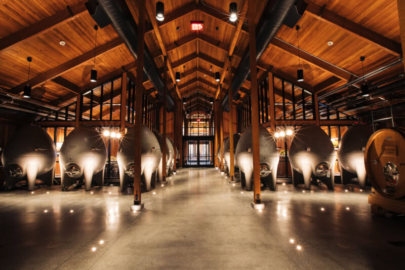 Artisan wine fermentation tanks inside a modern winery with warm wooden ceiling and industrial lighting.
