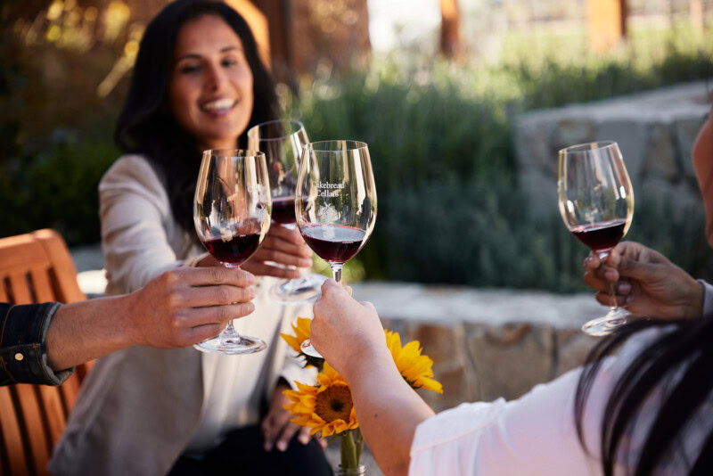 Group of friends clinking wine glasses outdoors at Cakebread Cellars, enjoying a wine tasting experience.