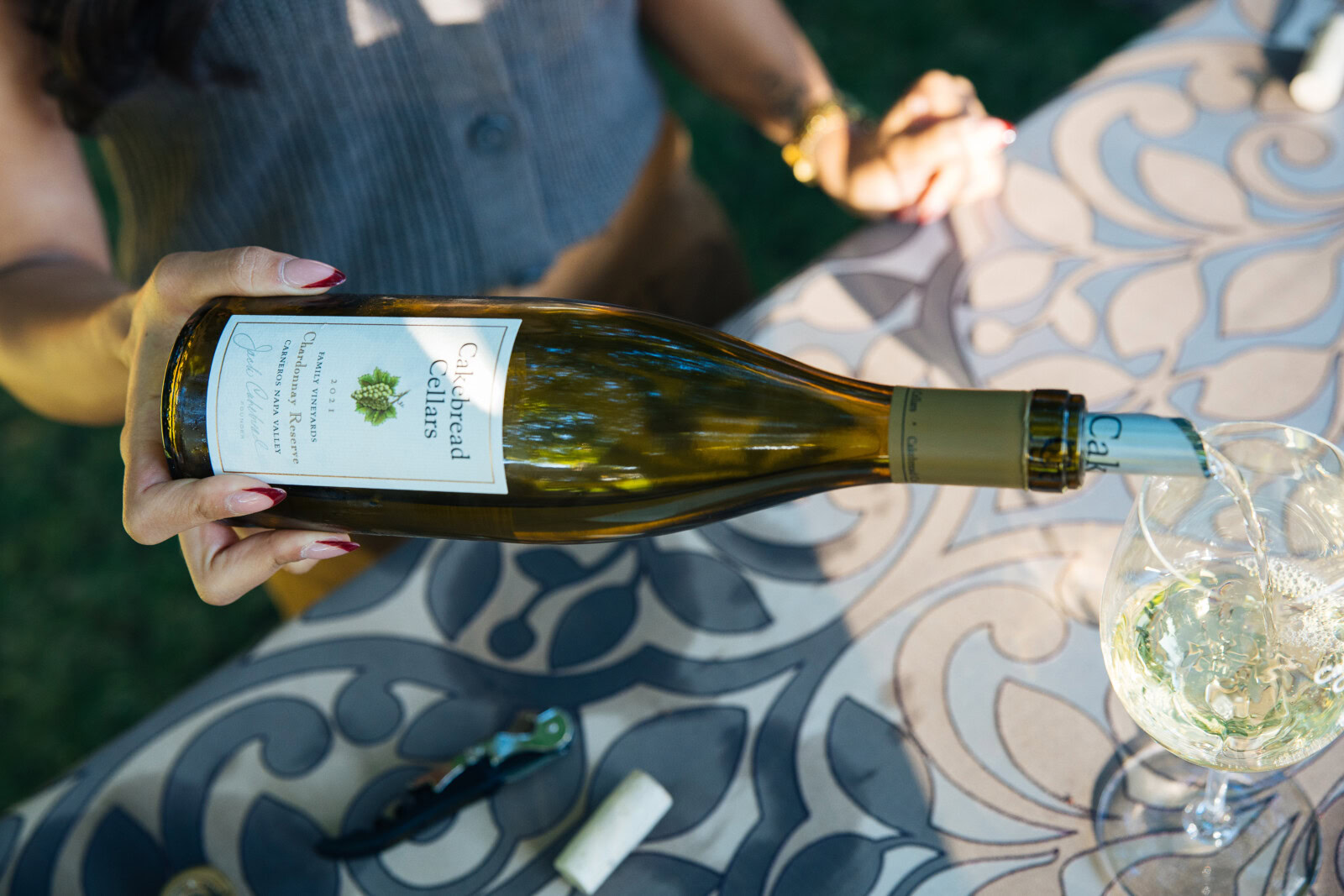 A bottle of Cakebread Cellars wine being poured into a glass on a decorative table.