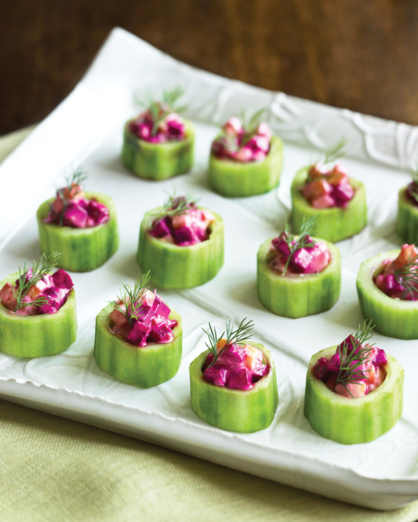 cucumber slices topped with cut beets and yogurt with sprigs of dill on a white square plate