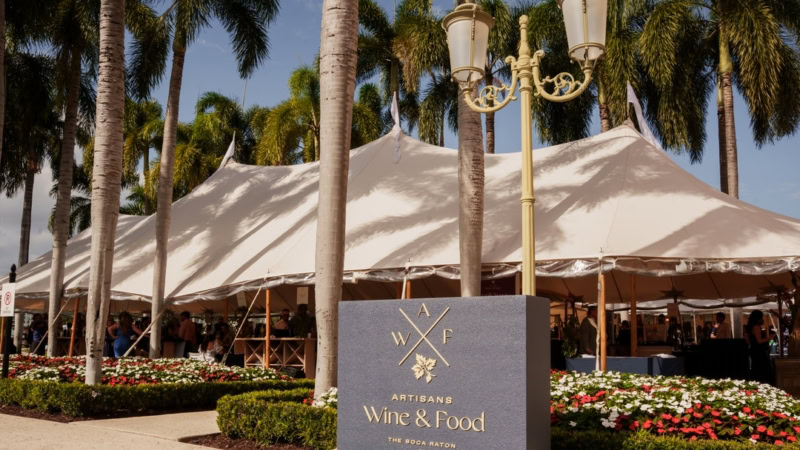 Outdoor event at Cakebread Cellars with a large white tent, palm trees, and a sign for Artisans of Wine & Food.