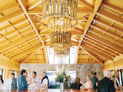 Guests enjoying a wine tasting event at Cakebread Cellars with a wooden ceiling and floral centerpiece.